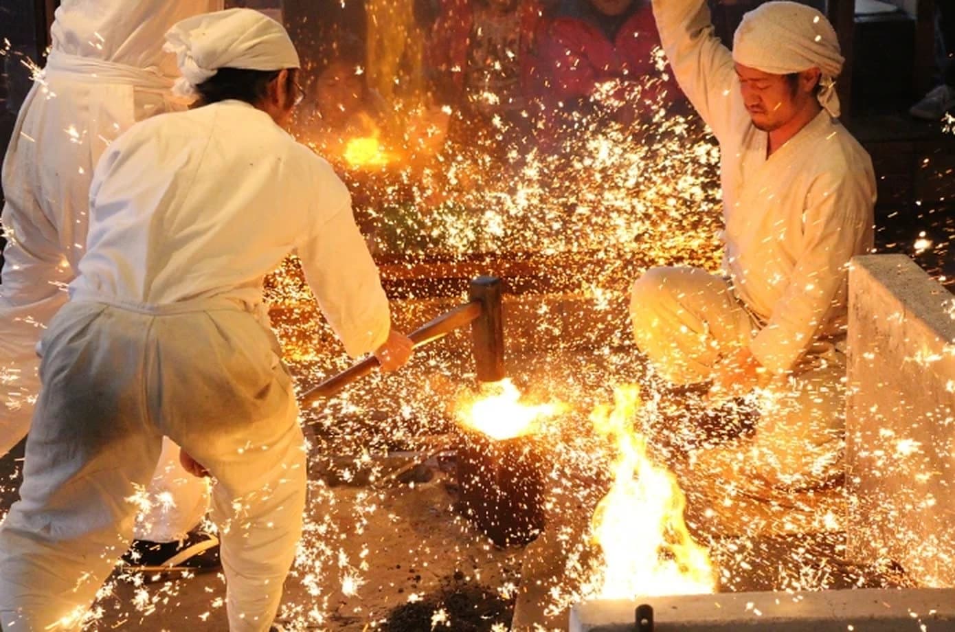 Two smiths in white striking glowing steel with a sledge, sparks bursting in every direction